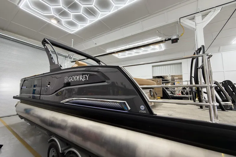 Slide: The Image of 2026 Godfrey Sanpan 25' Tritoon boat in showroom, featuring sleek design and modern amenities. - 7