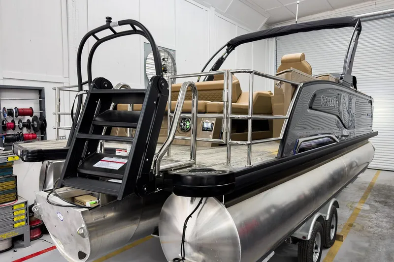 Slide: The Image of 2026 Godfrey Sanpan 25' Tritoon with flip lounge, showcased in a garage setting. - 9