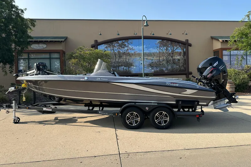 Slide: The Image of 2018 Triton 216 Fishunter boat on trailer, parked outdoors near a mural. - 0