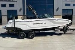 Slide: The Image of 2025 MasterCraft NXT22 boat on trailer, parked outside a modern building. - 13