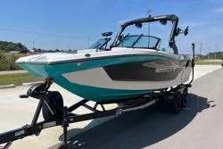 Slide: The Image of 2025 MasterCraft XT22 boat on trailer, teal and black design, parked outdoors. - 4