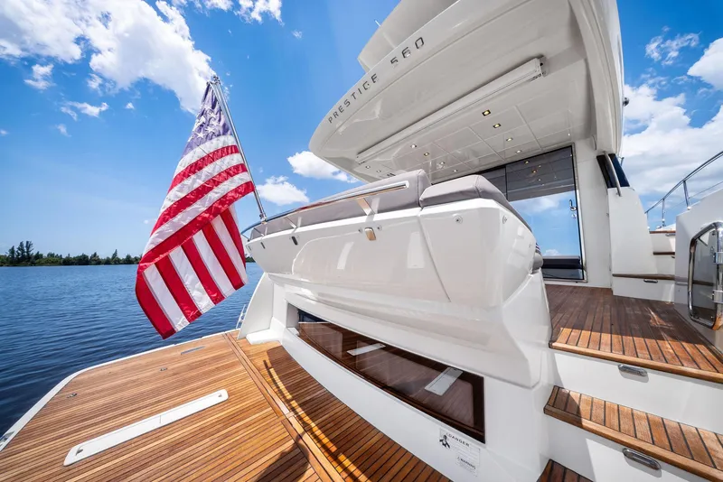 Slide: The Image of 2017 Prestige 560 Flybridge yacht with American flag, wooden deck, and clear blue sky. - 14
