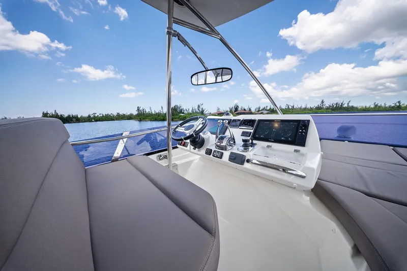 Slide: The Image of 2017 Prestige 560 Flybridge helm with modern controls, overlooking serene water and blue sky. - 24