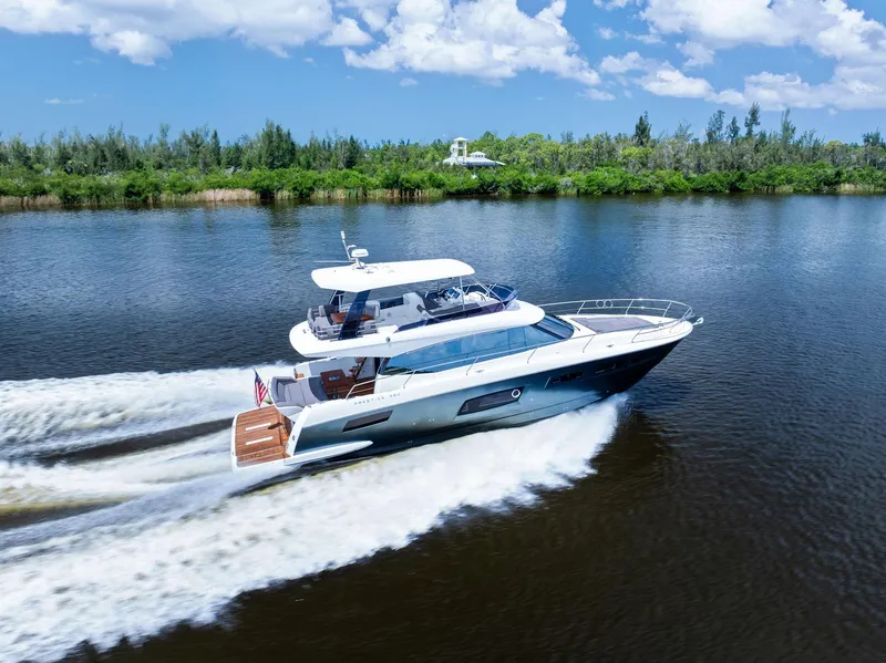 Slide: The Image of 2017 Prestige 560 Flybridge yacht cruising on a scenic river under a clear blue sky. - 4