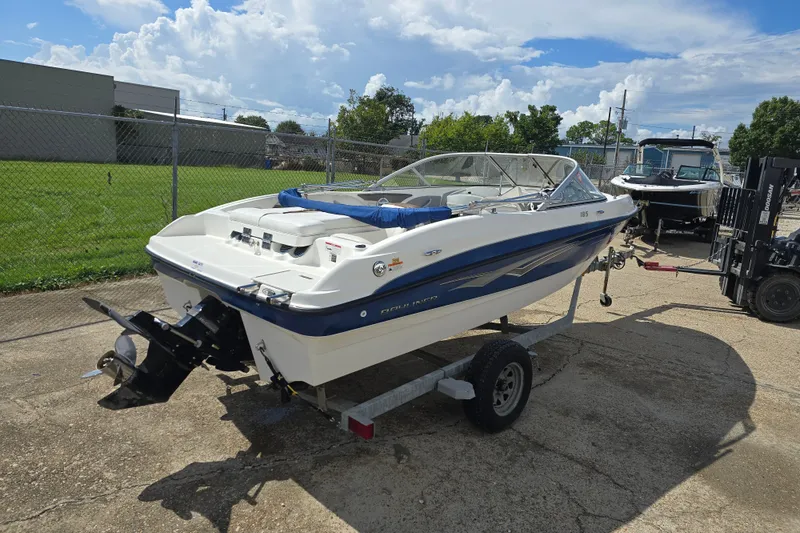Slide: The Image of 2010 Bayliner 185 Bowrider on trailer, parked outdoors under a partly cloudy sky. - 2