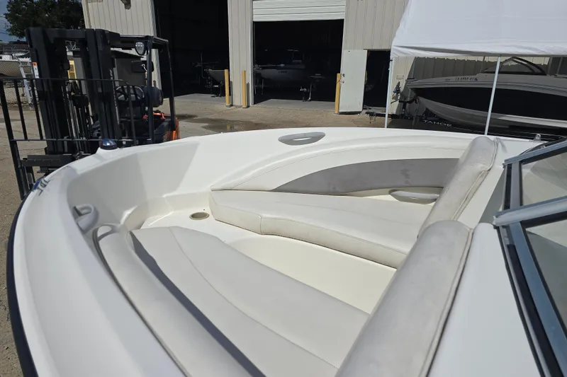 Slide: The Image of 2010 Bayliner 185 Bowrider boat interior with white seating, parked near a warehouse. - 7