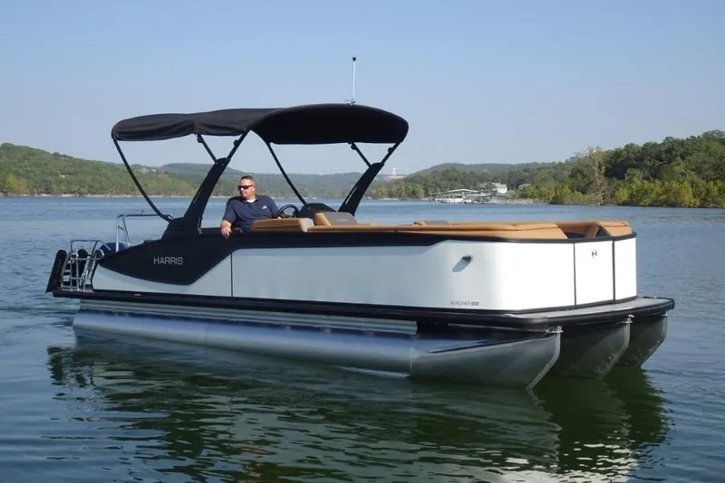 The Image of 2026 Harris Sunliner 250 pontoon boat on a serene lake with scenic background. - 0