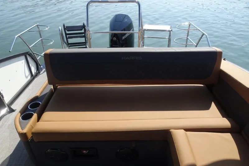 Slide: The Image of 2026 Harris Sunliner 250 boat with tan seating and cup holders on a calm lake. - 28