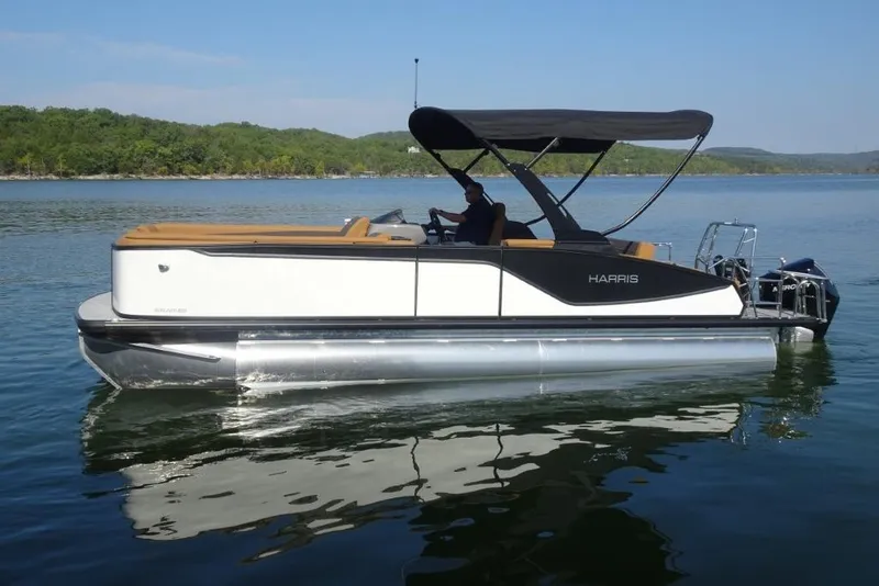Slide: The Image of 2026 Harris Sunliner 250 pontoon boat on a calm lake with lush green shoreline. - 4