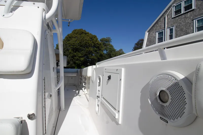 Slide: The Image of 2015 Edgewater 245CC boat interior with white seating and speaker, near a house. - 8