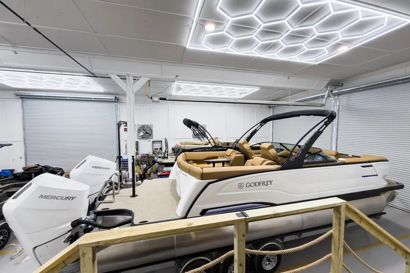 Slide: The Image of 2026 Godfrey Sanpan 27' Tritoon in a modern garage with Mercury engines. - 6