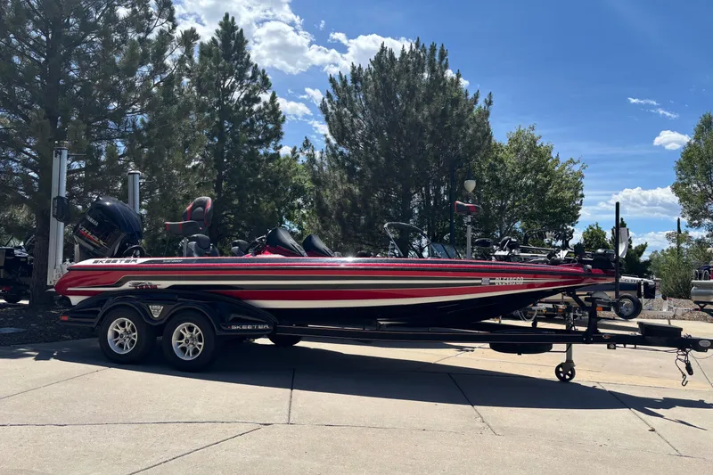 The Image of 2017 Skeeter FX21 bass boat on trailer, parked outdoors with trees in background. - 0