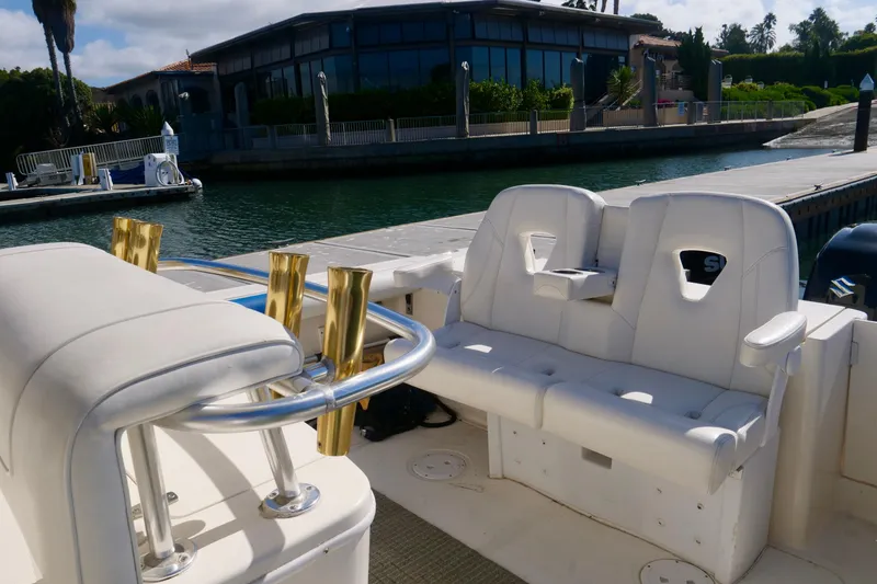 Slide: The Image of 1999 Pursuit 2870 Walkaround boat interior with white seating and gold rod holders at dock. - 12
