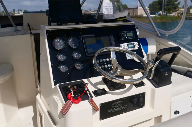 Slide: The Image of 1999 Pursuit 2870 Walkaround boat dashboard with steering wheel and navigation instruments. - 15