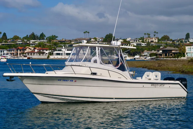 Slide: The Image of 1999 Pursuit 2870 Walkaround boat on water, coastal homes in background, clear sky. - 2