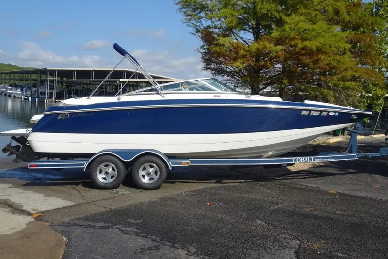 Slide: The Image of 2003 Cobalt 24SD boat on trailer by lakeside with trees in background. - 2