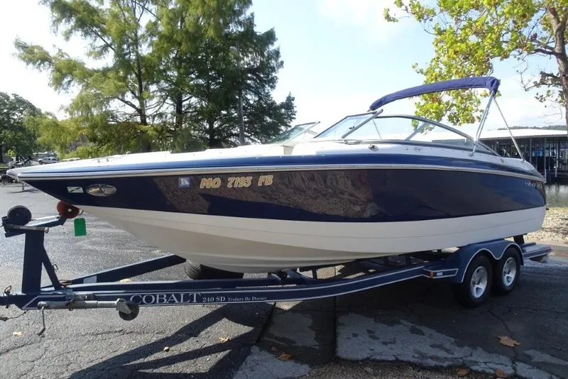 Slide: The Image of 2003 Cobalt 24SD boat on trailer, parked outdoors with trees in background. - 7