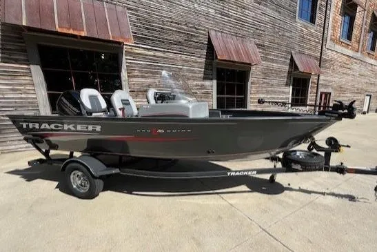 The Image of 2019 Tracker Pro Guide V-16 SC fishing boat on trailer, parked outside rustic building. - 0