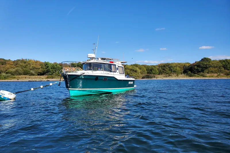 Slide: The Image of 2025 Ranger Tugs R23 boat moored on a serene lake under a clear blue sky. - 2