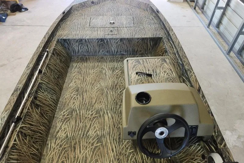 Slide: The Image of 2026 Tracker Grizzly 1648 SC boat with camouflage interior design in a garage setting. - 4