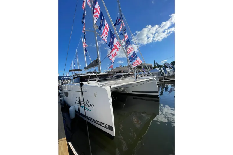 Slide: The Image of 2023 Fountaine Pajot Tanna 47 catamaran docked with flags, under clear blue sky. - 17