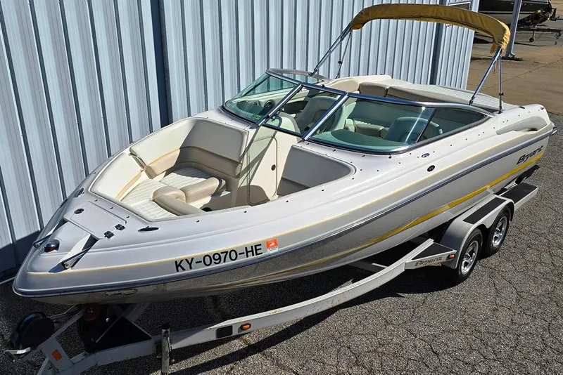 The Image of 2007 Bryant 219 BR boat on trailer, white with yellow accents, parked by metal building. - 0