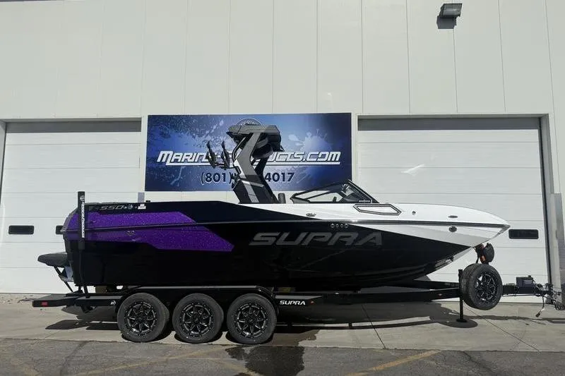 The Image of 2025 Supra SE 575 boat with black and purple design on a trailer. - 1