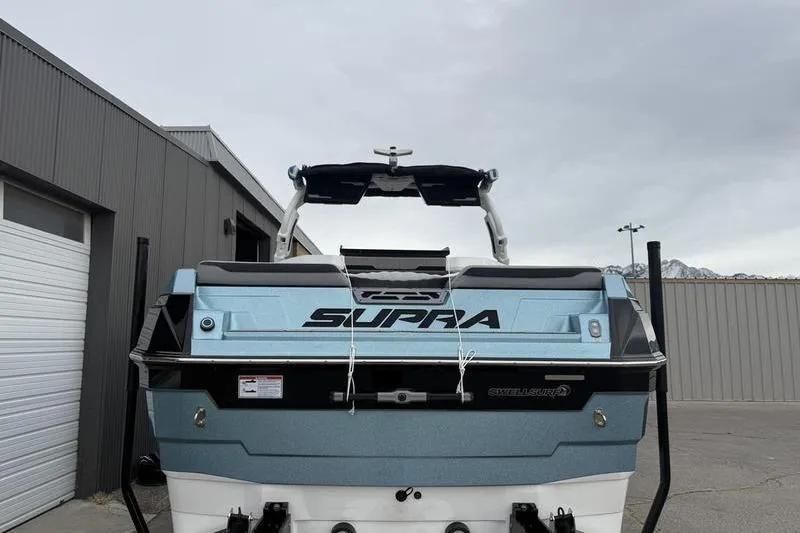 Slide: The Image of 2025 Supra SE 575 boat, rear view, parked near industrial buildings. - 2