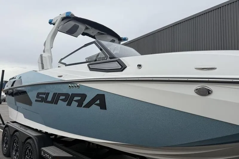 Slide: The Image of 2025 Supra SE 575 boat on trailer, sleek design, blue and white exterior. - 3