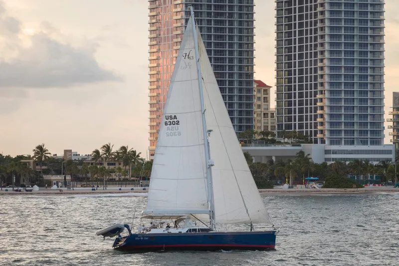 Slide: The Image of Sailboat Hylas 63 (2013) cruising near modern high-rise buildings at sunset. - 13