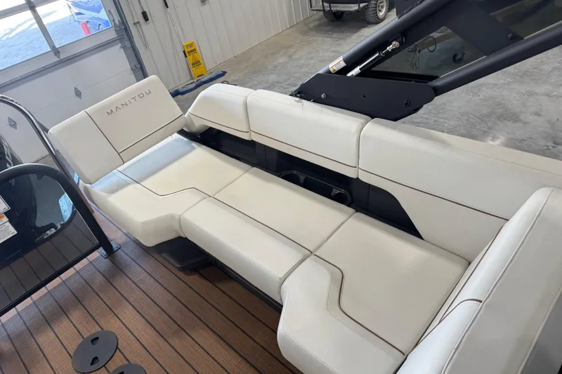 Slide: The Image of 2025 Manitou 26 Explore boat interior with white seating in a garage setting. - 10