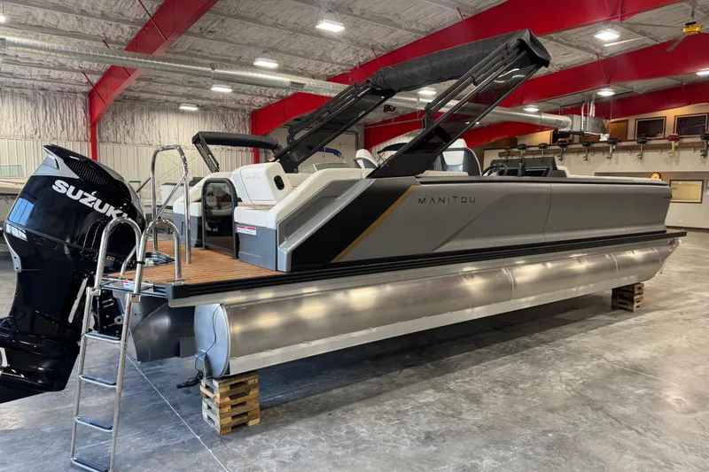 Slide: The Image of 2025 Manitou 26 Explore pontoon boat with Suzuki outboard motor in a warehouse setting. - 4