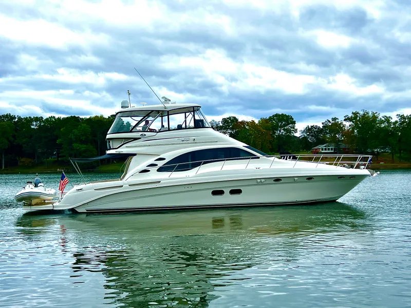 The Image of 2009 Sea Ray 58 Sedan Bridge yacht cruising on a scenic lake under a clear blue sky. - 0