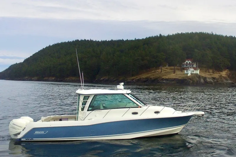 The Image of 2021 Boston Whaler 345 Conquest Pilothouse on calm water near a forested shoreline. - 0