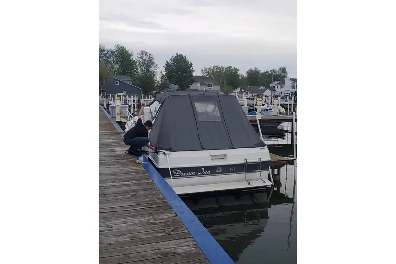 Slide: The Image of 1988 Trojan 8.6 Meter Mid-Cabin boat docked, person securing cover, overcast day. - 3