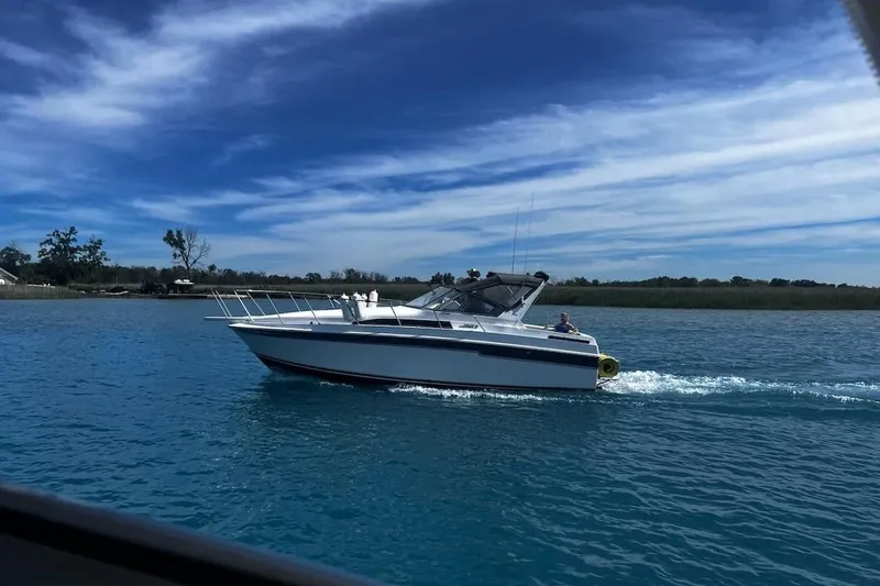 Slide: The Image of 1988 Trojan 8.6 Meter Mid-Cabin boat cruising on a clear blue lake under a vibrant sky. - 2