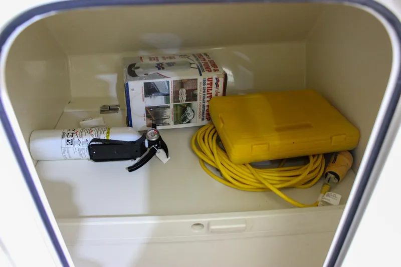 Slide: The Image of Storage compartment in 2018 Chris-Craft Calypso 30 with fire extinguisher, yellow cable, and utility pump. - 52