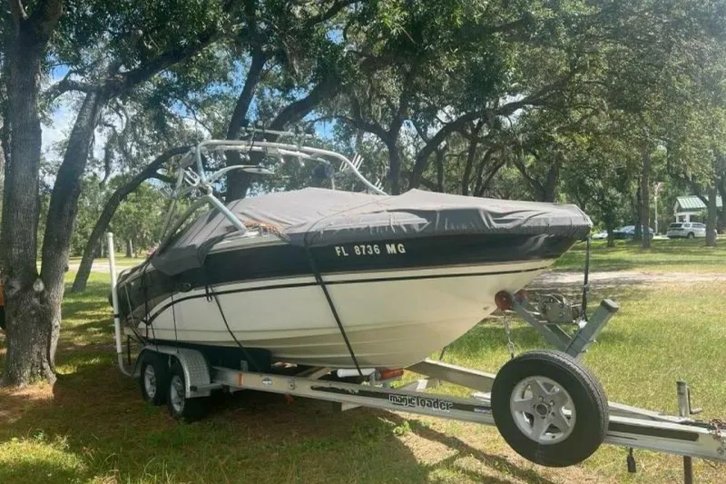 Slide: The Image of 2003 Sea Ray 220 Bow Rider boat on trailer, covered, parked under trees. - 11