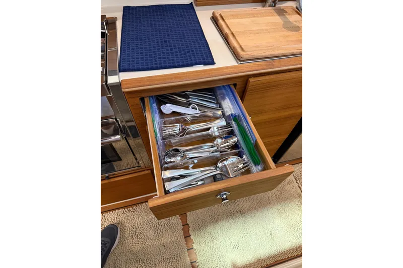 Slide: The Image of Drawer with utensils in 2025 Ranger Tugs R-27 kitchen, featuring wooden cabinetry and cutting board. - 14
