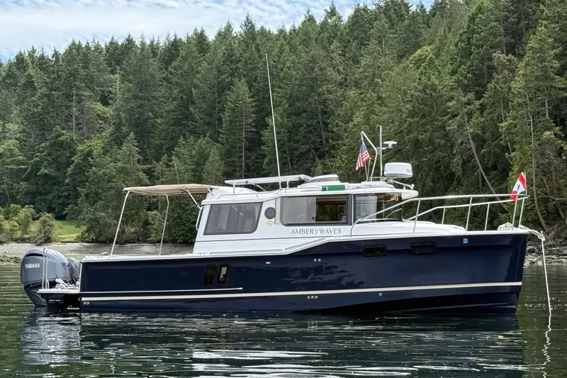 Slide: The Image of 2025 Ranger Tugs R-27 boat on calm water, surrounded by lush green forest. - 2