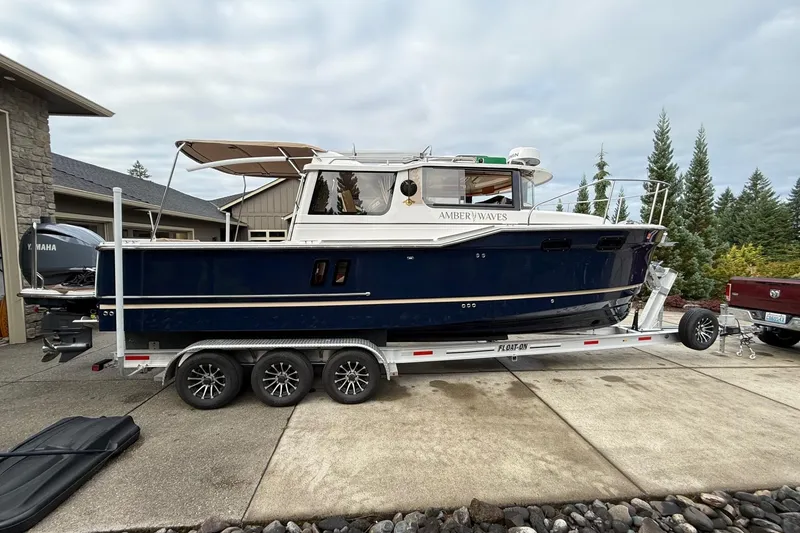 Slide: The Image of 2025 Ranger Tugs R-27 boat on trailer, parked in driveway, surrounded by trees. - 3