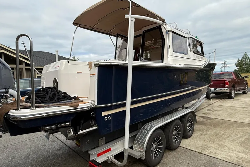 Slide: The Image of 2025 Ranger Tugs R-27 boat on trailer, parked outdoors, with a pickup truck nearby. - 4