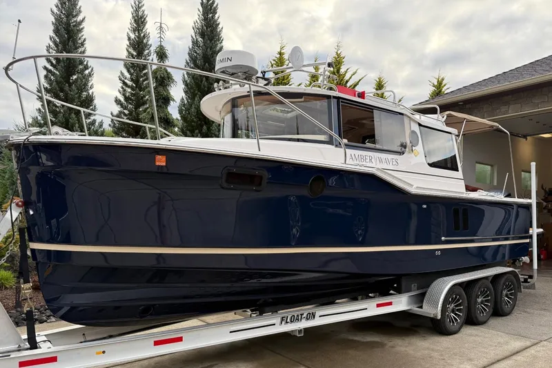 Slide: The Image of 2025 Ranger Tugs R-27 boat on trailer, navy blue hull, parked outdoors. - 6