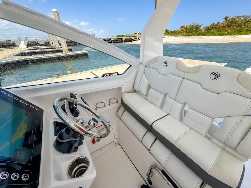 Slide: The Image of 2025 Edgewater 262 CX boat interior with white seating and steering wheel, dockside view. - 10