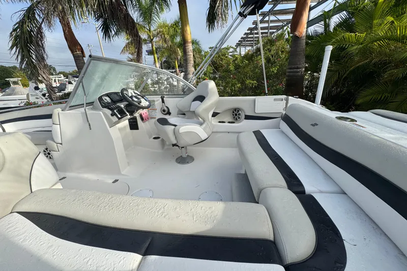 Slide: The Image of 2019 Starcraft MDX 210 OB boat interior with seating and steering console, surrounded by palm trees. - 17