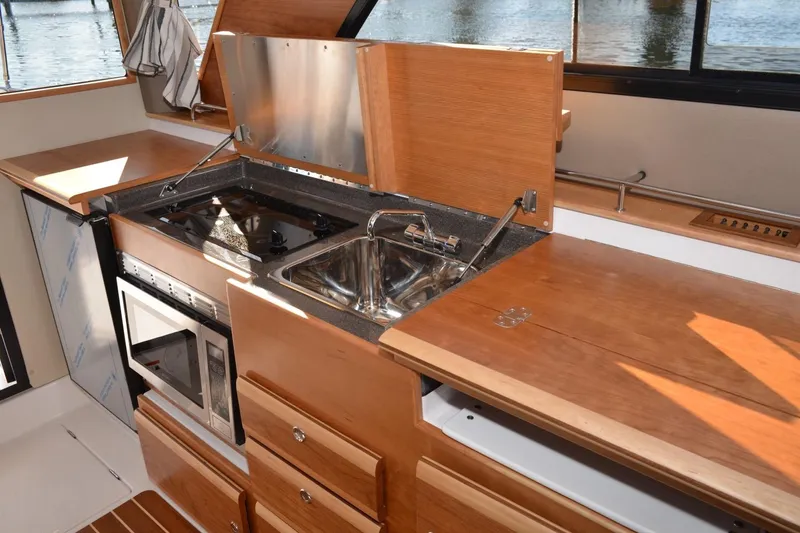 Slide: The Image of 2020 Cutwater C-30S boat kitchen with stove, sink, and microwave, featuring wooden cabinetry. - 14