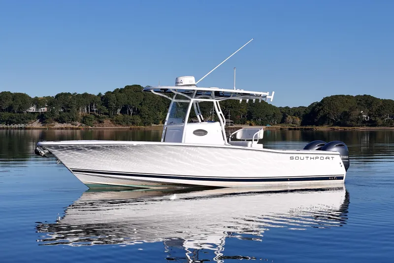 The Image of 2019 Southport 272 TE boat on calm water, clear sky, forested shoreline. - 0