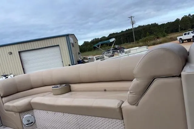 Slide: The Image of 2012 Tahoe Pontoon VT 2285 EL with beige seating, parked near a warehouse. - 13