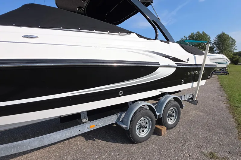 Slide: The Image of 2013 Rinker 276 Captina boat on trailer, black and white design, parked outdoors. - 2