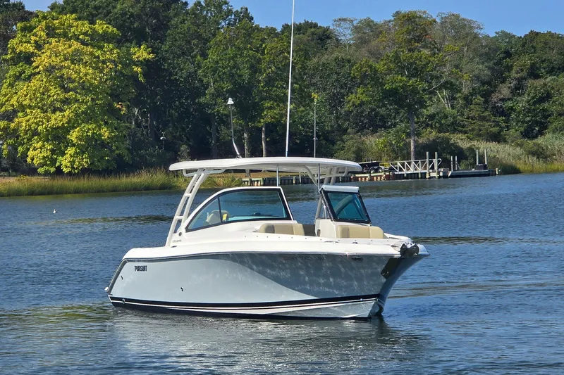 Slide: The Image of 2020 Pursuit DC 235 Dual Console boat on a serene lake with houses in the background. - 2